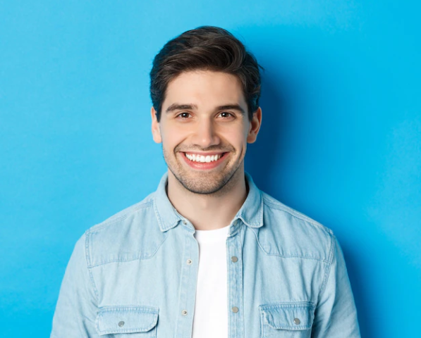 Free Photo Close up of young successful man smiling at camera standing in casual outfit against blue background